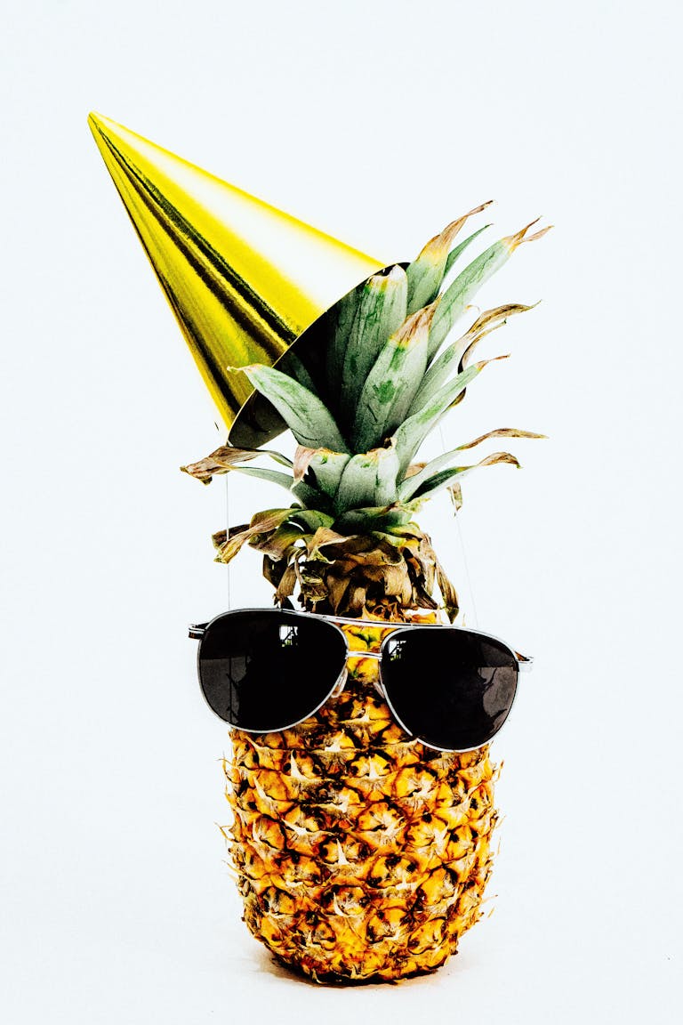 Ananas ubrany w okulary przeciwsłoneczne i imprezowy kapelusz, emanujący zabawą i tropikalnym klimatem.